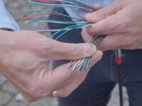 Bauleiter (m/w/d) Tiefbau Glasfaserausbau Ein Mann fächert bunte Glasfaserröhrchen auf.